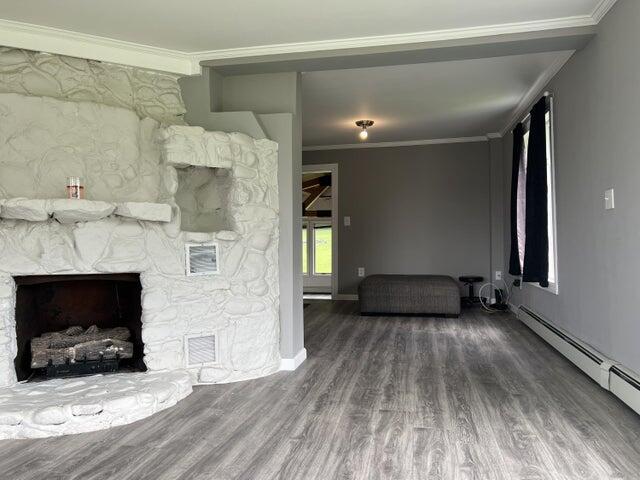 unfurnished living room featuring a baseboard heating unit, a stone fireplace, ornamental molding, and wood-type flooring