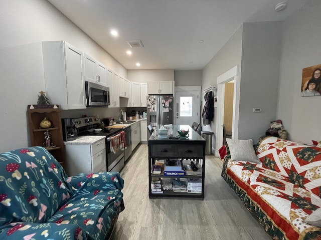 kitchen with light hardwood / wood-style floors, light stone countertops, appliances with stainless steel finishes, white cabinets, and sink
