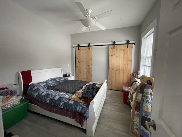 bedroom with ceiling fan, dark hardwood / wood-style flooring, and a barn door