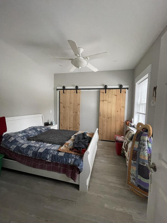 bedroom with dark hardwood / wood-style floors, ceiling fan, and a barn door