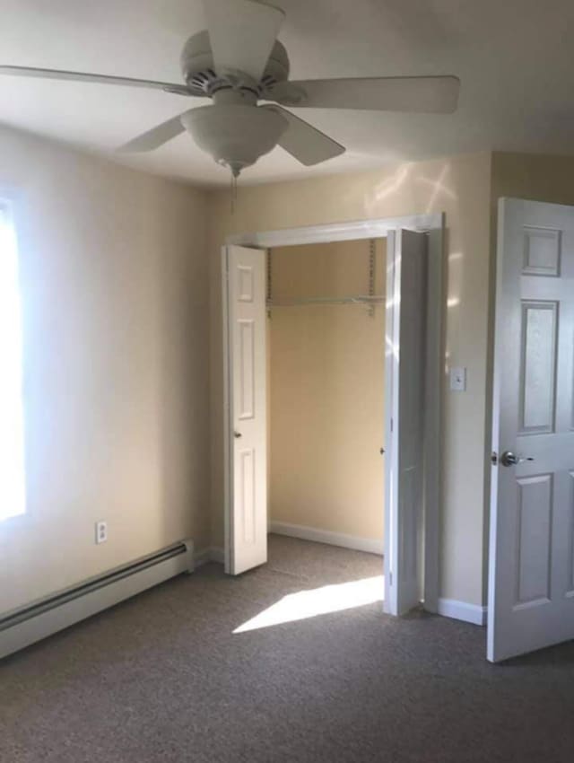unfurnished bedroom with a closet, ceiling fan, a baseboard heating unit, and dark colored carpet