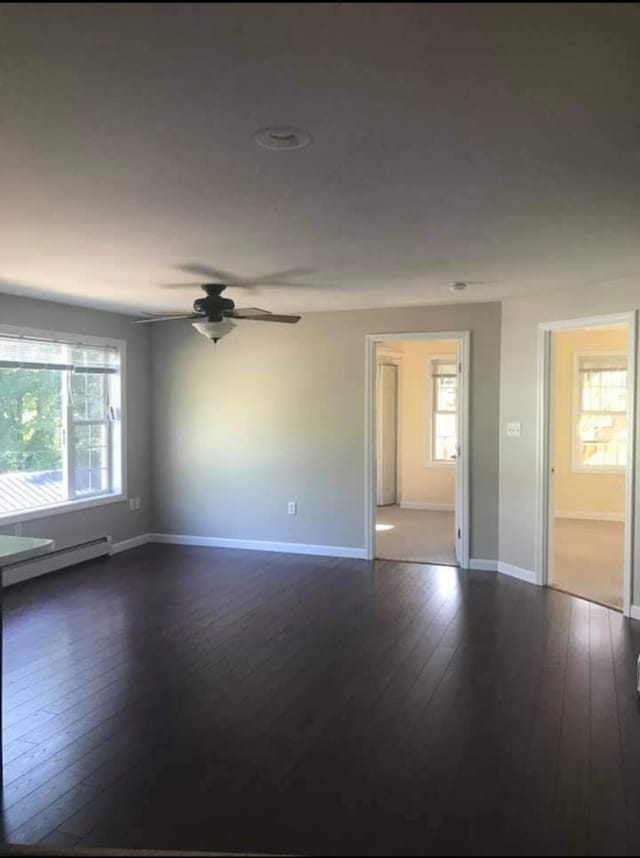 spare room featuring ceiling fan, baseboard heating, and dark hardwood / wood-style floors