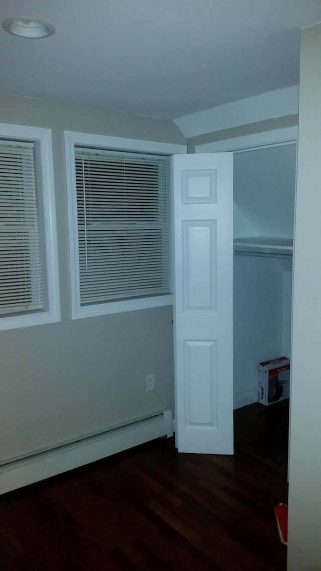 unfurnished bedroom featuring a closet, a baseboard heating unit, and dark wood-type flooring