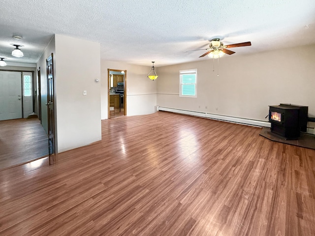 unfurnished living room with a baseboard radiator, ceiling fan, a wood stove, hardwood / wood-style floors, and a textured ceiling