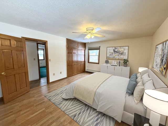 bedroom featuring light hardwood / wood-style floors, a textured ceiling, a baseboard radiator, a closet, and ceiling fan