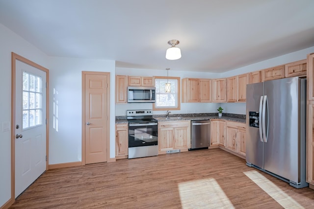 kitchen featuring light brown cabinetry, decorative light fixtures, stainless steel appliances, and light hardwood / wood-style floors