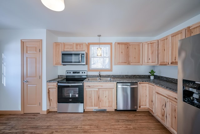 kitchen with stainless steel appliances, light brown cabinetry, hanging light fixtures, and sink