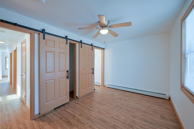 unfurnished bedroom with ceiling fan, a baseboard heating unit, a barn door, and light wood-type flooring