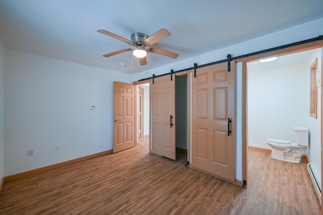 unfurnished bedroom featuring a barn door, ceiling fan, ensuite bath, light wood-type flooring, and baseboard heating