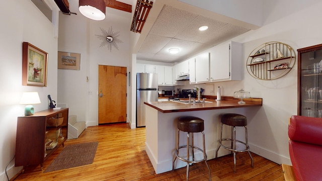 kitchen featuring light hardwood / wood-style flooring, a breakfast bar area, stainless steel appliances, white cabinets, and kitchen peninsula