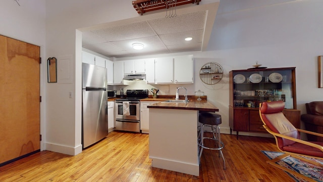 kitchen featuring a breakfast bar area, wooden counters, appliances with stainless steel finishes, white cabinets, and kitchen peninsula