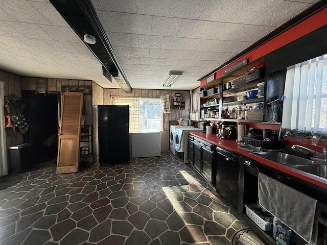 kitchen featuring sink, wood walls, black fridge, and washing machine and dryer