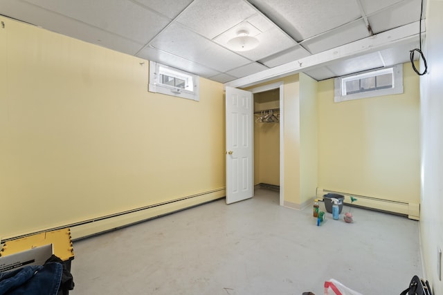 basement with a paneled ceiling and baseboard heating