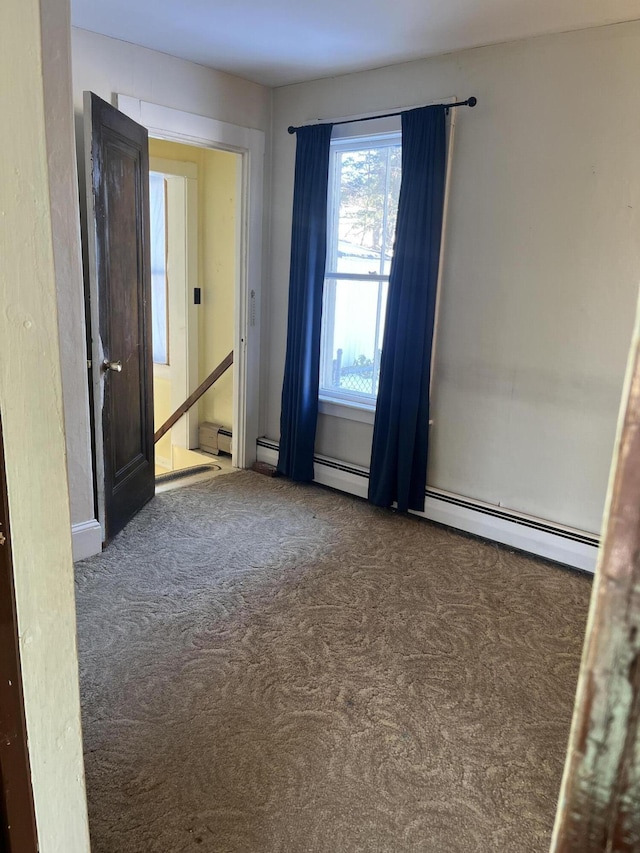 empty room featuring a baseboard heating unit and dark carpet