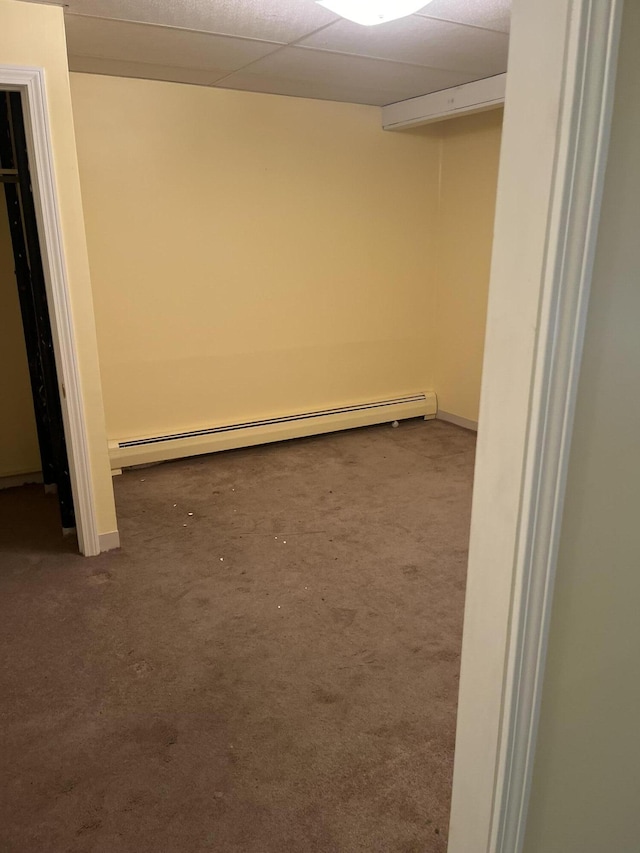 basement featuring a baseboard heating unit, a drop ceiling, and dark colored carpet