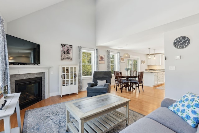 living area featuring high vaulted ceiling, light wood-style flooring, and a tile fireplace