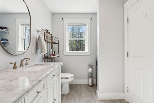 bathroom featuring baseboards, toilet, wood finished floors, and vanity