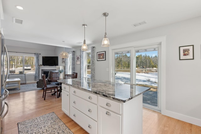 kitchen with visible vents, light wood-style flooring, a fireplace, and dark stone counters