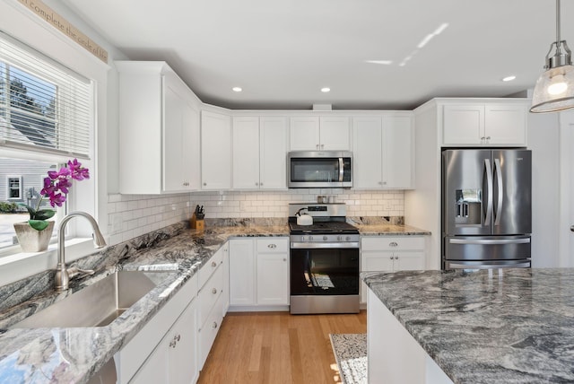 kitchen with a sink, tasteful backsplash, white cabinetry, appliances with stainless steel finishes, and light wood finished floors