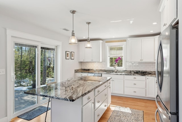 kitchen featuring light wood finished floors, freestanding refrigerator, stone countertops, white cabinetry, and a sink