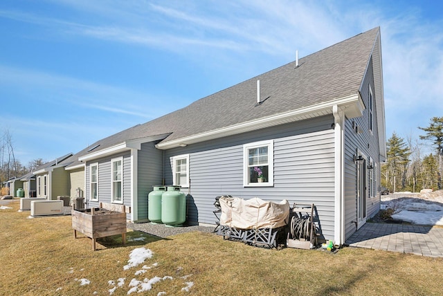 rear view of house featuring central AC unit, a lawn, and roof with shingles