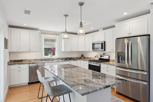 kitchen featuring visible vents, a sink, stainless steel appliances, white cabinets, and light wood-style floors