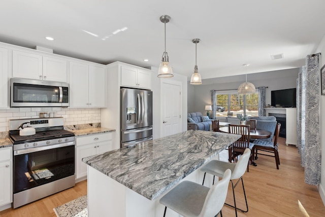 kitchen with tasteful backsplash, light wood finished floors, open floor plan, and appliances with stainless steel finishes