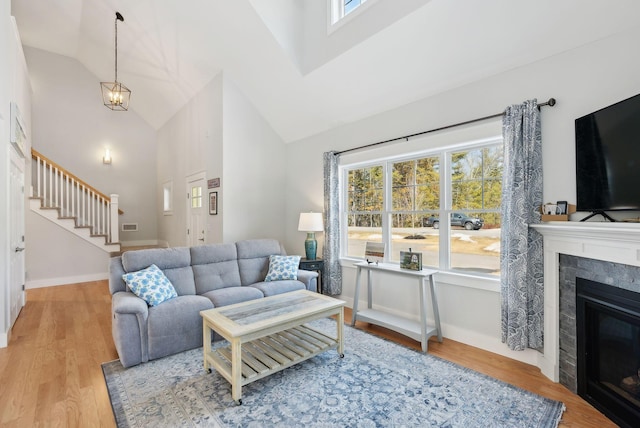 living area featuring baseboards, stairs, a tile fireplace, wood finished floors, and high vaulted ceiling