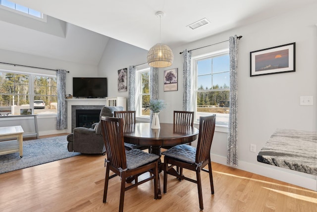 dining area featuring visible vents, light wood-style flooring, a tile fireplace, and vaulted ceiling