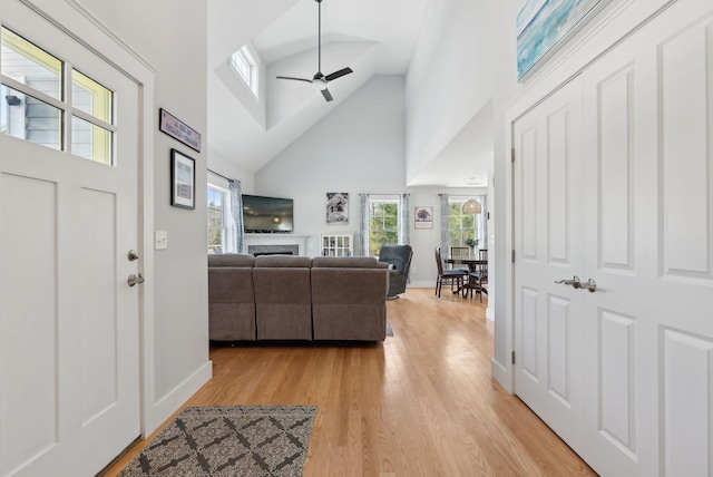 foyer featuring baseboards, light wood-style flooring, high vaulted ceiling, and ceiling fan