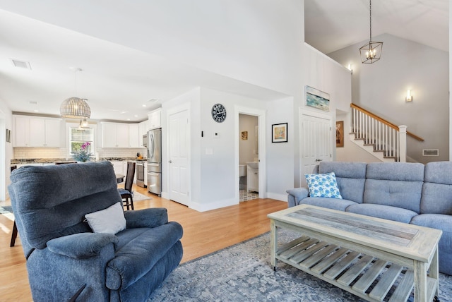 living room featuring stairway, visible vents, light wood finished floors, and high vaulted ceiling