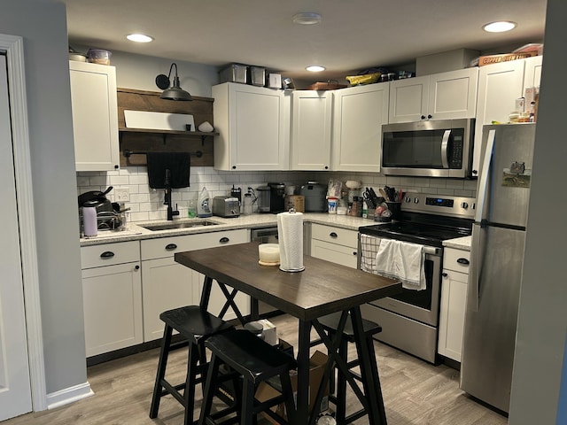 kitchen featuring sink, white cabinetry, appliances with stainless steel finishes, light hardwood / wood-style floors, and backsplash