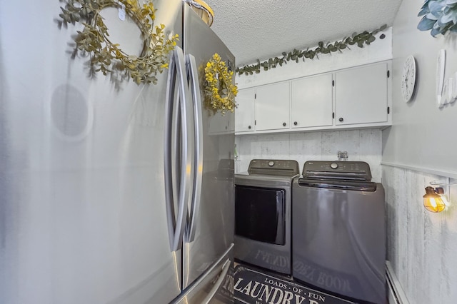 clothes washing area featuring a textured ceiling, washer and clothes dryer, a baseboard radiator, and cabinet space