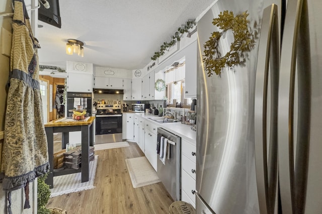 kitchen featuring light wood-style flooring, stainless steel appliances, light countertops, under cabinet range hood, and a sink