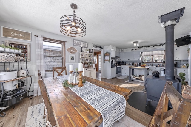 dining area with a wood stove, a healthy amount of sunlight, a notable chandelier, and wood finished floors