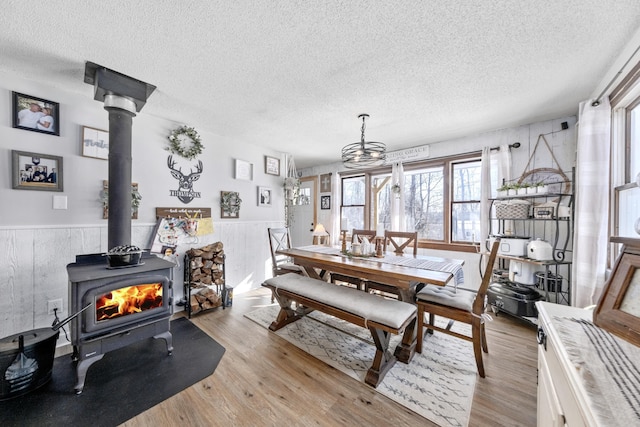 dining area with a wood stove, a wainscoted wall, a textured ceiling, and light wood-style floors