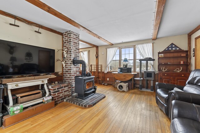 living room with beamed ceiling, light hardwood / wood-style floors, and a wood stove