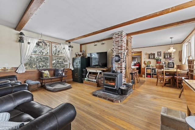 living room with beamed ceiling, a wood stove, and light hardwood / wood-style flooring