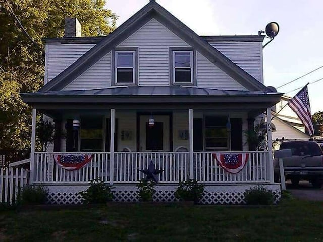 view of front of property with a standing seam roof, metal roof, covered porch, a front lawn, and a chimney