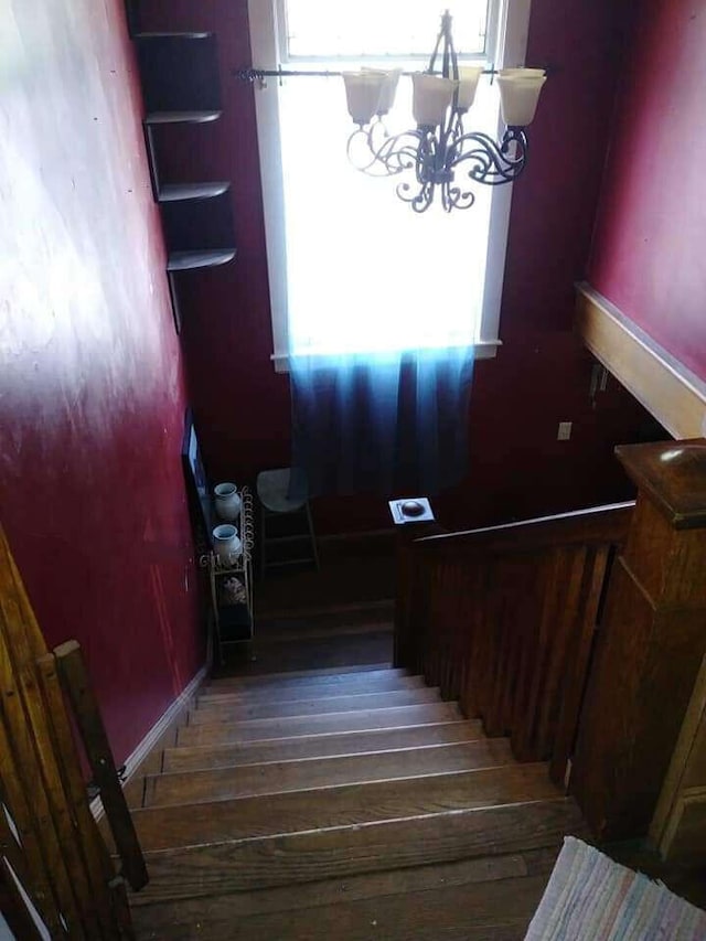 stairway featuring a notable chandelier, a healthy amount of sunlight, and wood finished floors