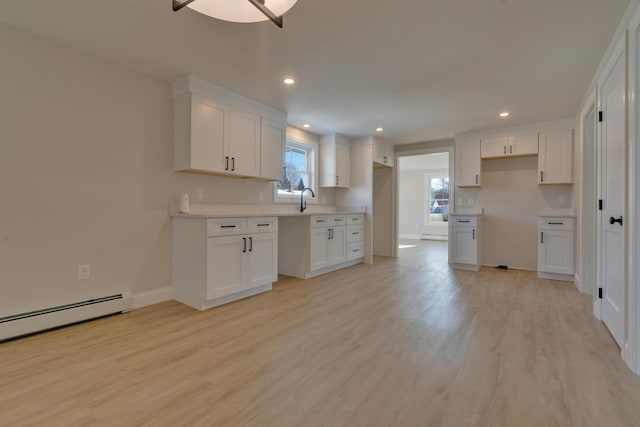 kitchen featuring sink, baseboard heating, light wood-type flooring, and white cabinetry