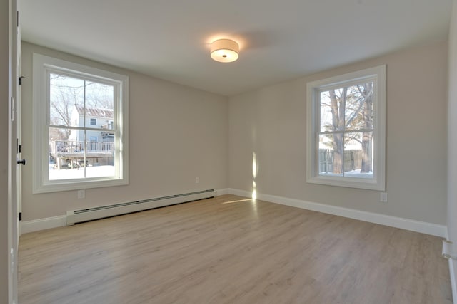 empty room featuring a baseboard heating unit, light hardwood / wood-style floors, and plenty of natural light