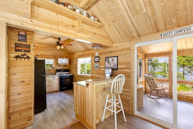 kitchen with light hardwood / wood-style flooring, light brown cabinetry, range with gas cooktop, a breakfast bar, and black fridge
