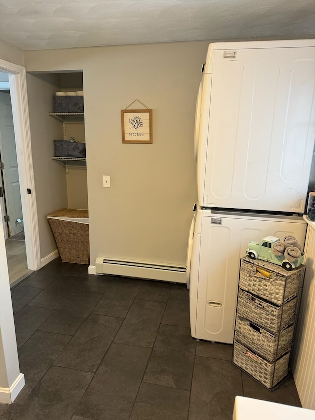 washroom with dark tile patterned floors, a baseboard radiator, and stacked washer / drying machine