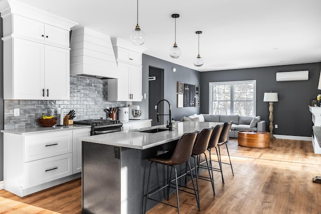 kitchen with custom exhaust hood, an AC wall unit, sink, white cabinets, and stainless steel gas range oven