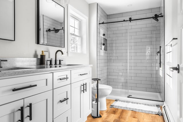 bathroom featuring toilet, hardwood / wood-style floors, walk in shower, baseboard heating, and vanity