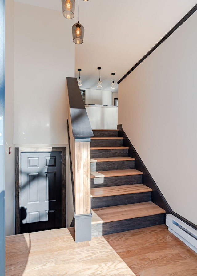 stairway featuring hardwood / wood-style flooring, a baseboard heating unit, and ornamental molding