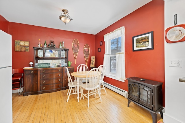 dining room with a baseboard heating unit, hardwood / wood-style floors, and a wood stove