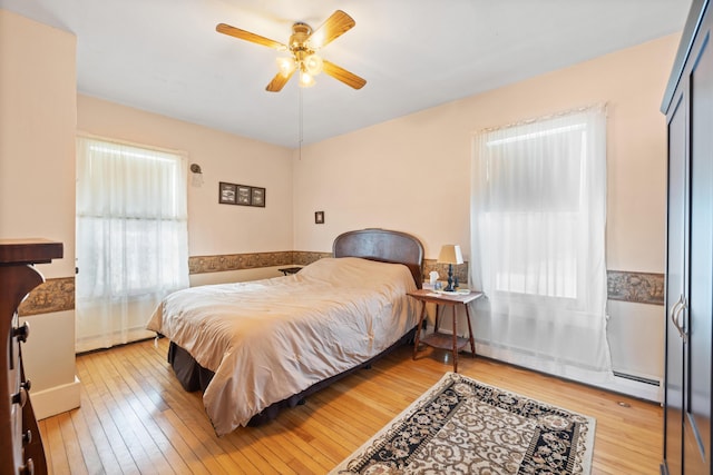 bedroom featuring ceiling fan, light hardwood / wood-style floors, and a baseboard heating unit