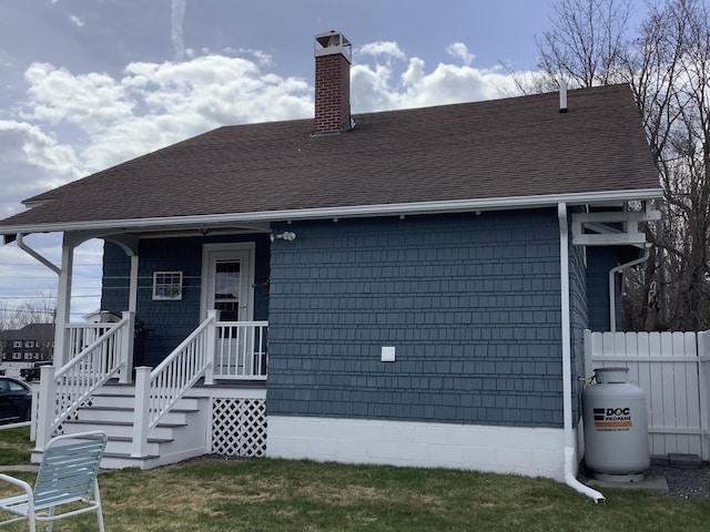 view of front of house featuring a chimney, roof with shingles, and fence